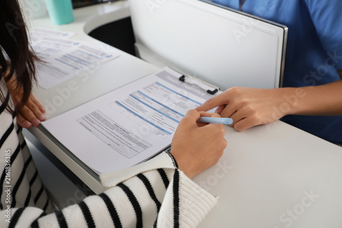 Medical intern with patient filling out health insurance at reception in clin...