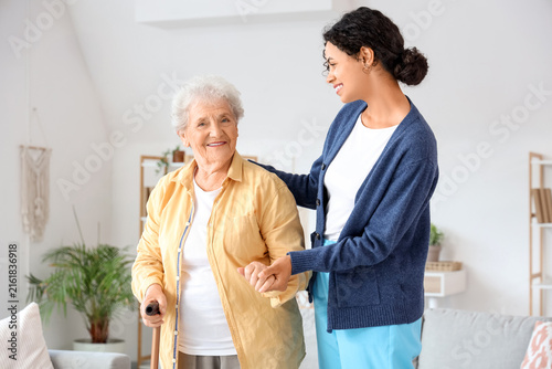 Young African-American female medical worker helping elderly woman in nursing...
