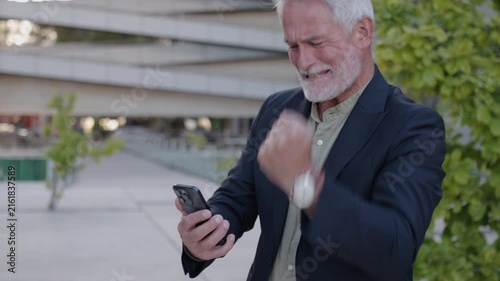 Happy senior businessman reacts to a smartphone message after closing a profitable business deal or winning a jackpot. Success, achievement, and financial reward concept.