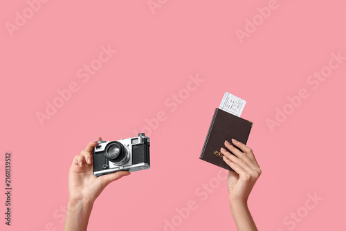 Female hands with passport and photo camera on pink background. Travel concept