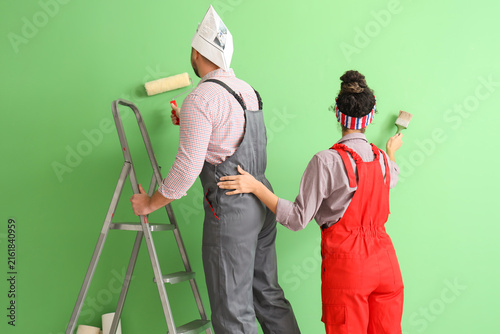 Obraz na płótnie Beautiful young couple with paint roller and brush near green wall doing repair