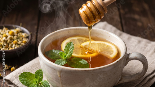 Cup of herbal tea with lemon and honey prepared on a wooden table in a cozy kitchen
