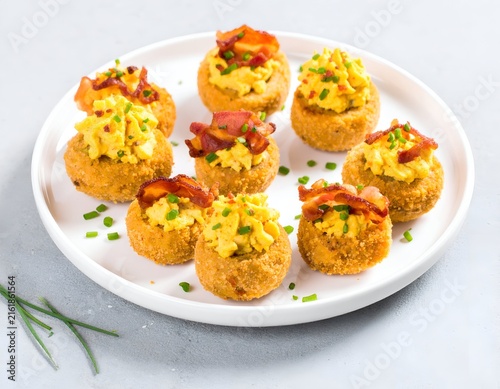 Golden, breaded deviled eggs with bacon and chives on a white plate