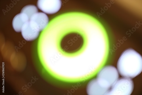 Close-up of glowing green ring with blurred white circular lights and warm brown background