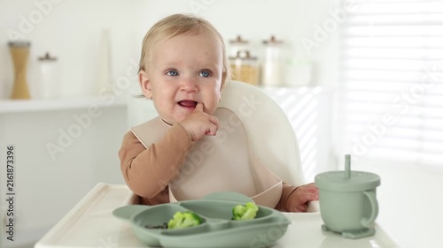 Baby tableware. Cute little child eating food from section plate on high chair at home