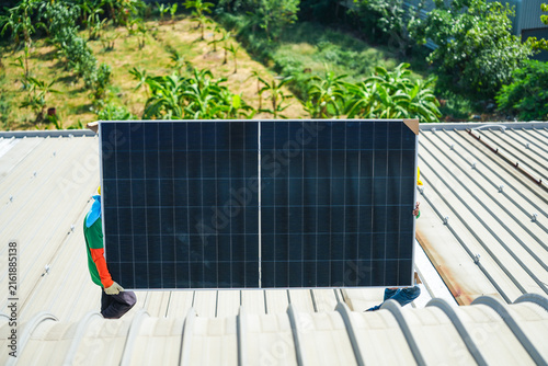 Foto A solar installation engineer in a white helmet and high visibility vest precisely carries a solar module flat along the very top of the curved roof high on an industrial warehouse roof