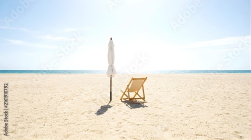 White beach umbrella and wooden chair on sunny sandy shore by ocean