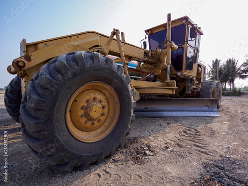 Cuadro en lienzo Low angle view of yellow motor grader machine working on dirt road leveling at construction site