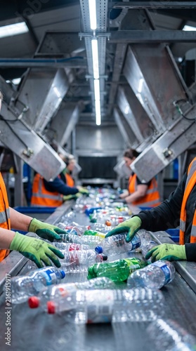 Workers in a recycling plant sort plastic bottles on a conveyor belt, showcasing the vital process of waste management and environmental conservation in an industrial setting.