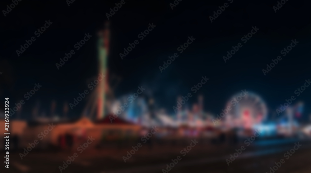 Fototapeta premium Abstract blurry night view of a colorful amusement park with glowing rides and ferris wheel.