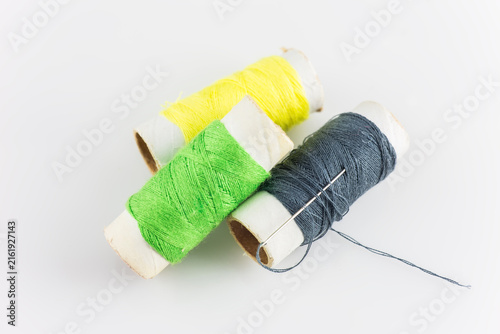Cuadro en lienzo Three colored thread spools and a sewing needle arranged on a plain white background, for sewing or craft use