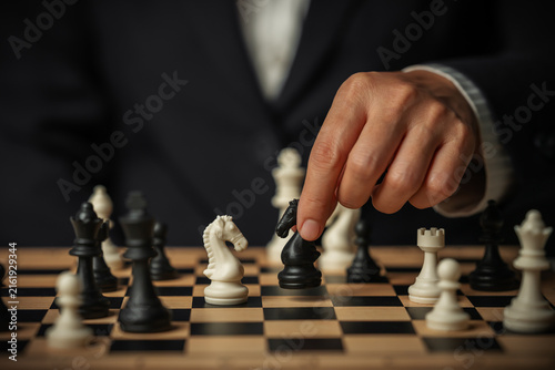 Картината върху платно business hand moving a black chess knight and white facing off on board with mul