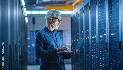 Professional IT technician using a laptop for server maintenance in a high-tech data center
