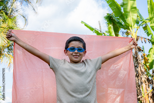 Принти на полотні Young boy playing dress-up, wearing blue sunglasses and a red cape, embracing im