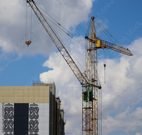 Bright yellow tower cranes rising against a clear blue sky, highlighting construction equipment and modern urban development. Construction site. Urbanization. Ust-Kamenogorsk (Kazakhstan)