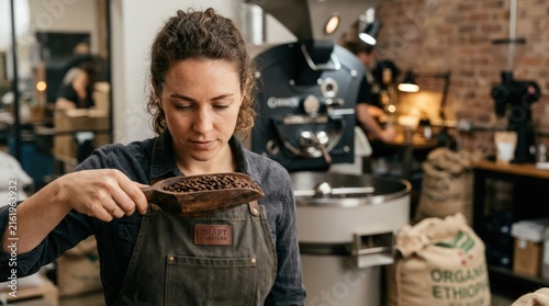 Female Coffee Roaster Inspecting Roasted Beans with Scoop in Roastery