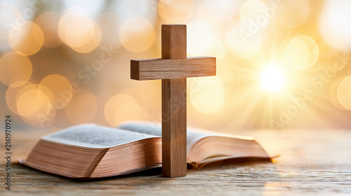 Wooden cross standing on an open Bible with a glowing, warm bokeh background.