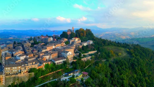 Sumptuous aerial truck right push-in shot from Santa Vittoria in Matenano, the town centre and its vintage buildings opening to a vision of a green promontory, full of thickets, typical Marche hills
