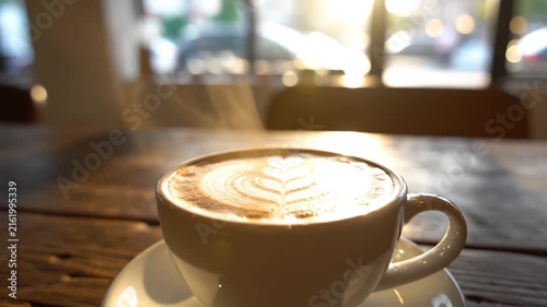 Steaming Latte Coffee Cup with Detailed Art on a Wooden Table in Warm Sunlight