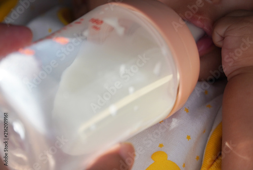 Obraz na płótnie Macro close-up of a baby's tiny hand holding a feeding bottle while drinking milk, focusing on delicate infant fingers, health care, formula nourishment, and gentle maternal care