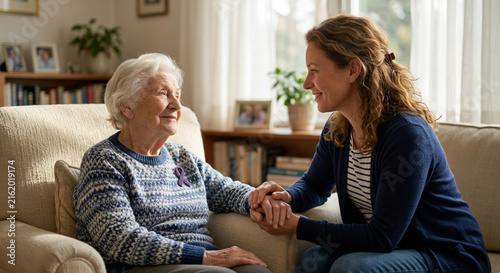 Caring daughter holding hands with her elderly mother sitting on a comfortable sofa at home.