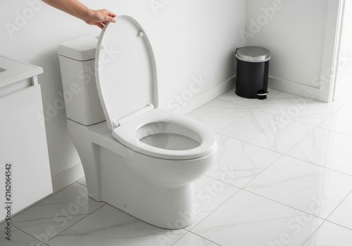 Hand opening the lid of a modern white ceramic toilet in a bright bathroom