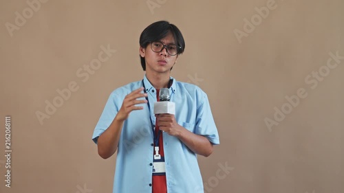 Young Asian male reporter holding microphone with stressed and touching his head while speaking in studio