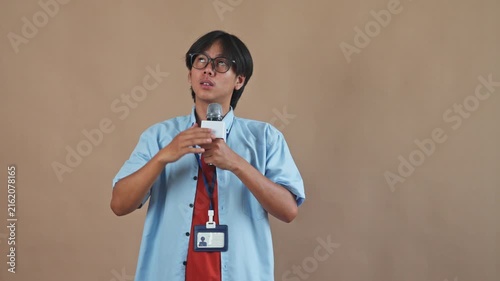 Asian male reporter holding microphone while placing hand above eyes to look into distance in studio setting