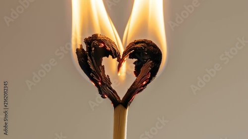 Burning matchstick shaped like a heart on a simple backdrop  