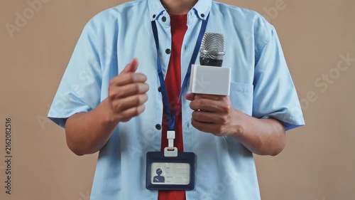 Medium shoot of Male reporter holding microphone and gesturing with his hand while speaking in studio