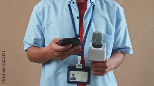 Midsection view of male reporter holding microphone and using smartphone in studio