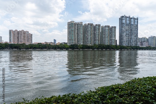 Bild auf Leinwand Tall buildings reflected in river under partly cloudy sky