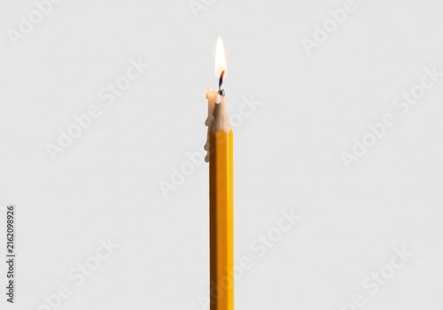 Burning yellow pencil with candle flame on white background