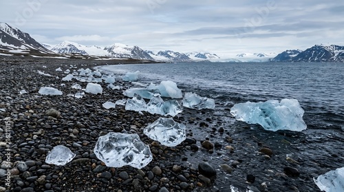 Blue Glacial Ice Chunks Scattered on Rocky Arctic Beach with Snowy Mountain Range and Cloudy Sky Background Landscape