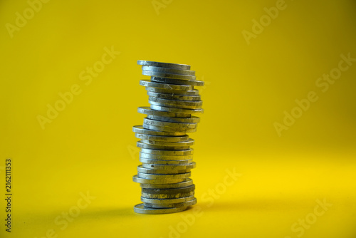 Cuadro en lienzo Studio shot of a tall, unstable stack of silver coins towers high isolated on a bright yellow background