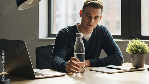 Young man drinking water while working on laptop