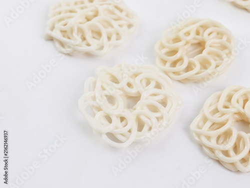 Macro top-down view of several raw, uncooked white kerupuk (Indonesian crackers) arranged neatly on a clean white background, showcasing their detailed noodle-like patterns and spiral textures.