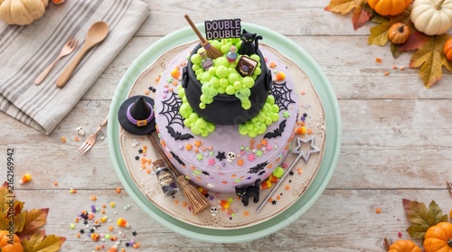 Elaborate Halloween witch's cauldron cake with purple frosting, green bubbles, black cats, and festive decorations on a wooden table with pumpkins.