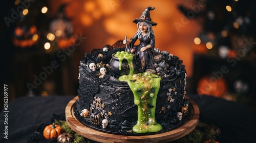 An elaborate black Halloween cake decorated with a witch figurine, a bubbling green cauldron, tiny skulls, and elegant black lace details.