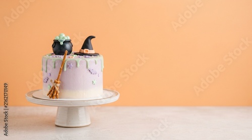 A whimsical Halloween-themed cake with purple frosting, green drip, a witch hat, cauldron, and pretzel broomstick on a white stand.
