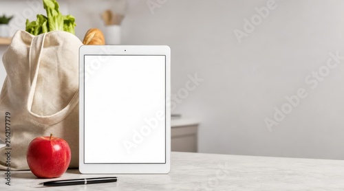 Kitchen island surface with blank white tablet and shopping bag