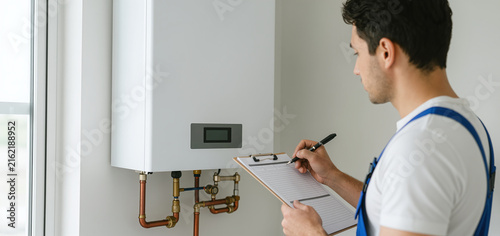 Technician holding clipboard writing report about water heater service inspection in home