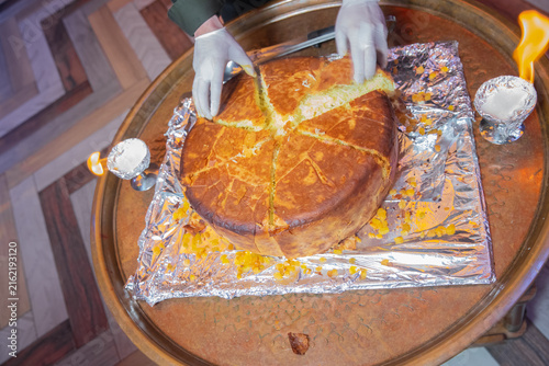 фотографія Chef cutting traditional shah plov baked in golden lavash crust during a fiery presentation on a tray