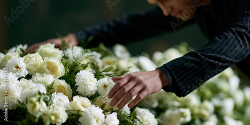 A person arranging a beautiful bouquet of white flowers, possibly for a memorial or special occasion. The hands gently touch the delicate petals, conveying a sense of care and solemnity