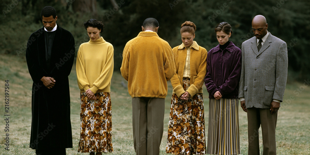 Fototapeta premium A group of six people standing in a line outdoors with their heads bowed, appearing to be in prayer or deep contemplation