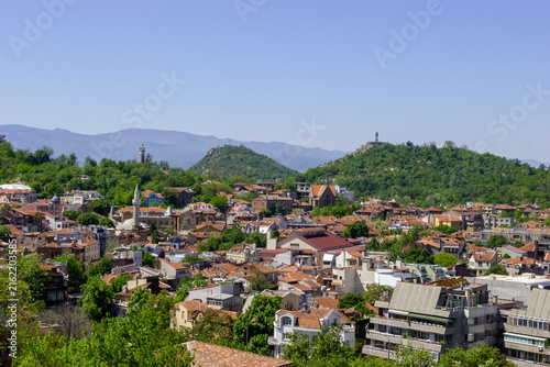 Cuadro en lienzo A panoramic view of the historic city of Plovdiv, Bulgaria, showcasing its distinctive red-tiled roofs, lush green hills, and ancient landmarks under a clear blue sky