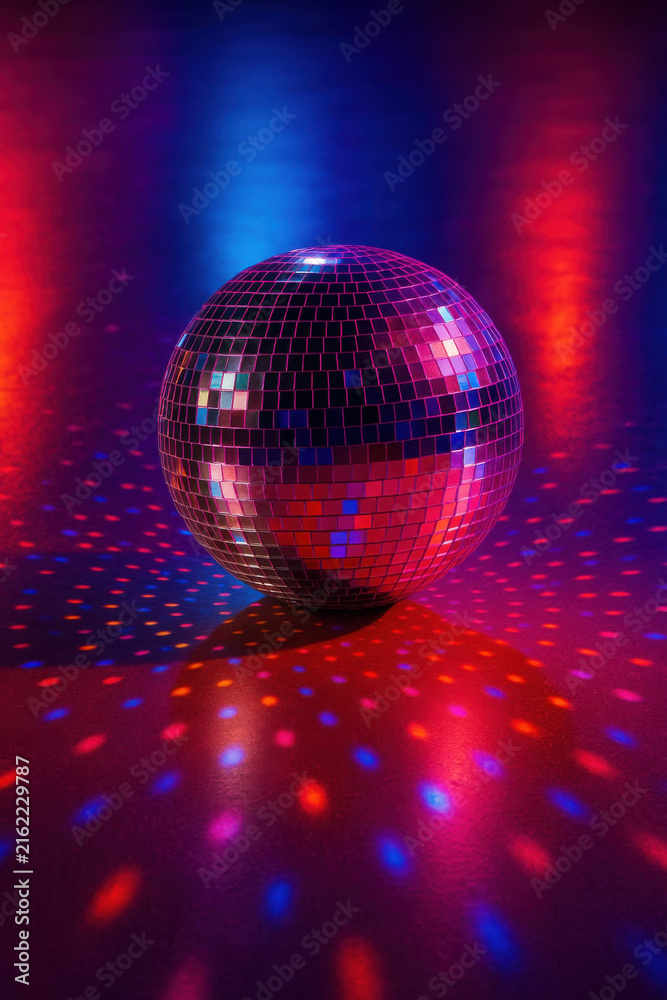 Fototapeta premium Disco ball reflecting colorful red and blue lights on dark dance floor creating vibrant party atmosphere with shiny mirrored surface and scattered light spots
