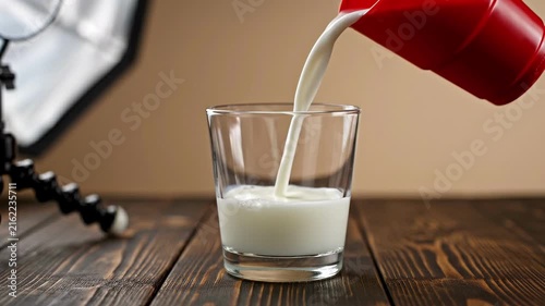 Pouring Fresh Milk Into A Clear Glass On A Wooden Table.