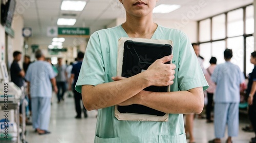 Emotional Thai Female Doctor Holding Tablet and Patient Chart in Hospital Corridor Showing Stress and Dedication in Healthcare