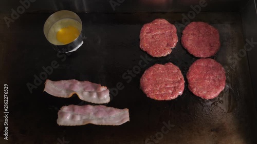 Close-up the chef is frying bacon, patties and eggs for burgers which are being prepared on a large stove in the restaurant kitchen.The process of making a juicy patty with bacon for a burger is shown